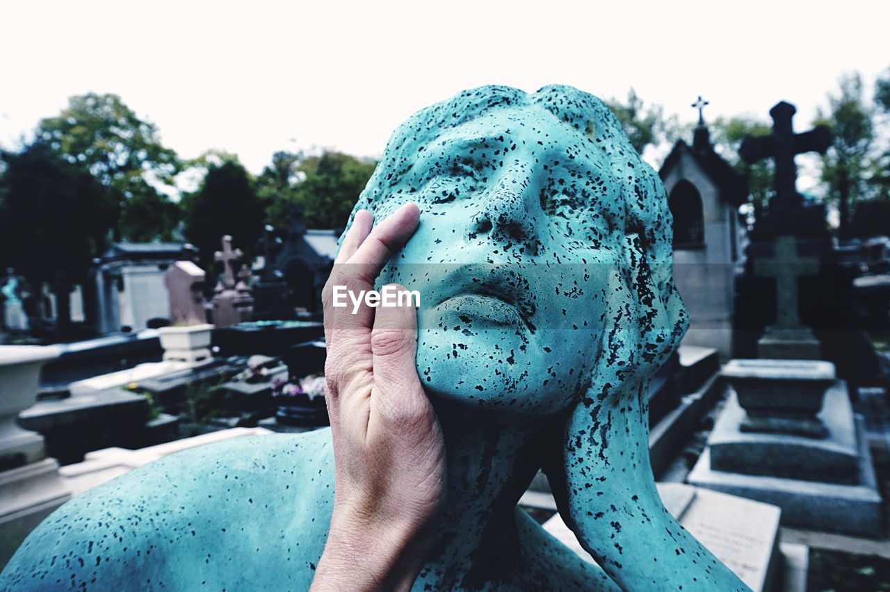 Cropped image of hand touching weathered stone sculpture in pere lachaise cemetery