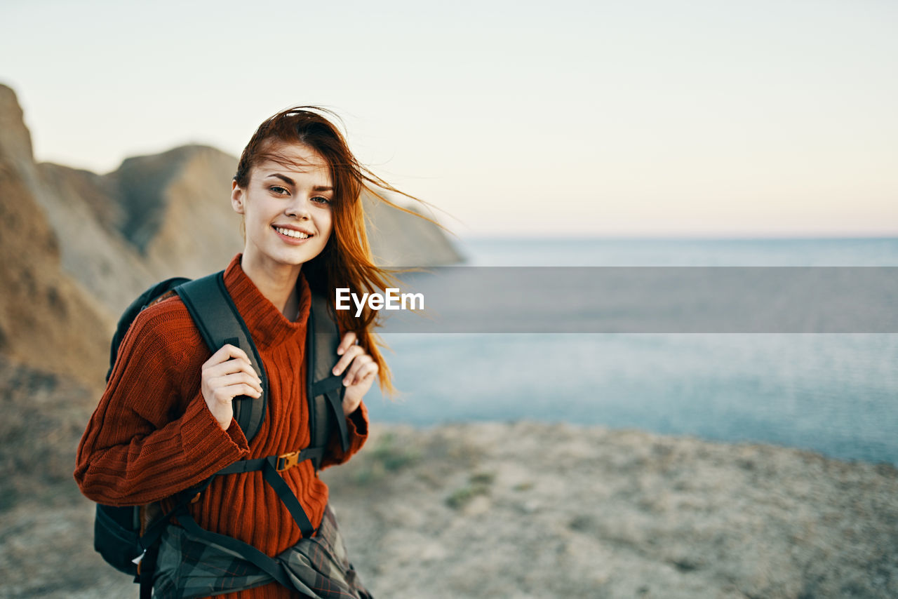 Portrait of smiling young woman standing in sea against sky