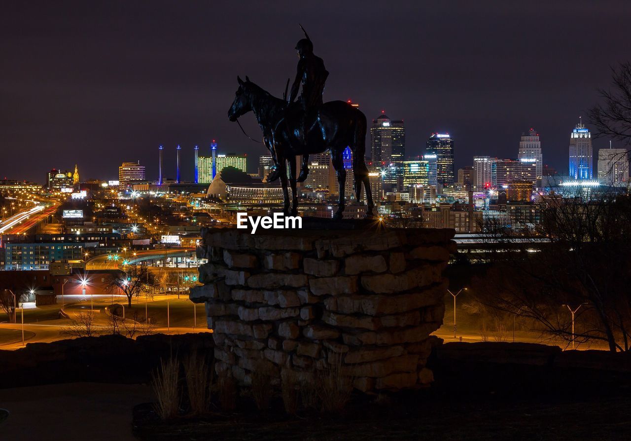 Statue against illuminated city at night