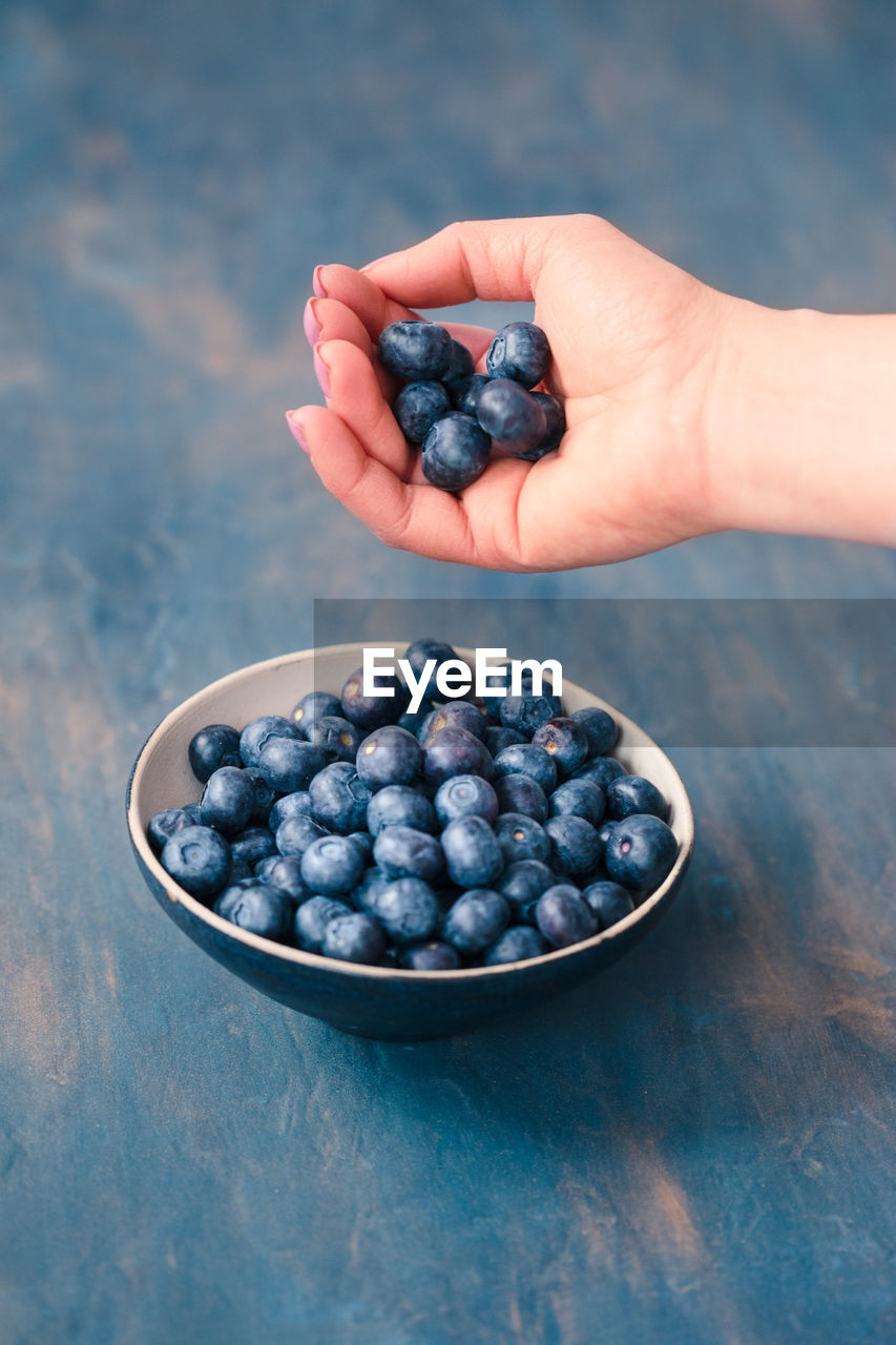 Cropped image of woman holding blueberries over bowl