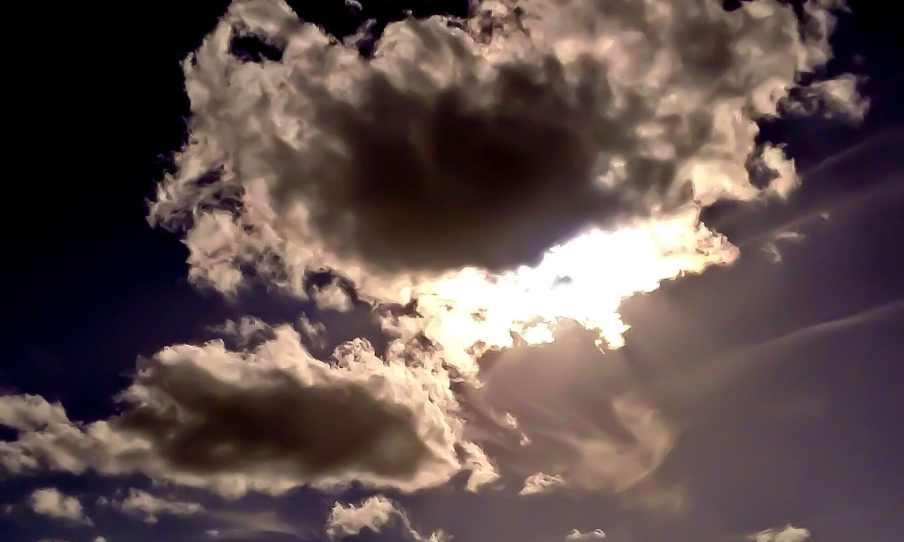 LOW ANGLE VIEW OF SUN SHINING THROUGH CLOUDS IN SKY