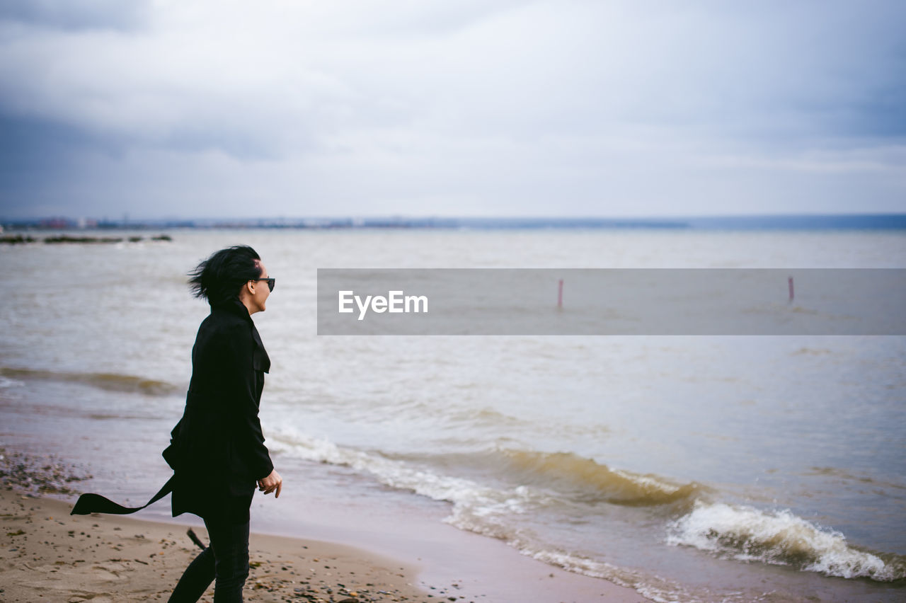 Woman walking at beach against sky