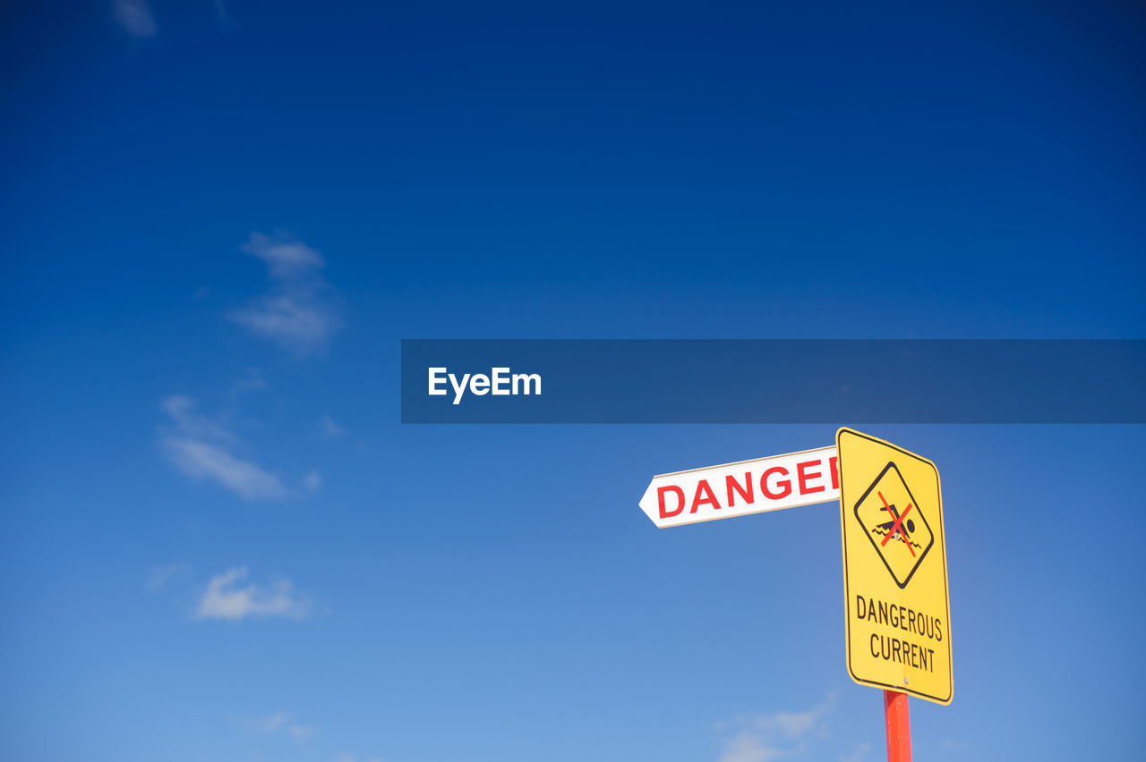 Low angle view of danger sign against sky