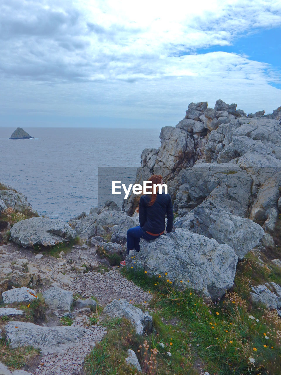 Rear view of men sitting on rock by sea against sky