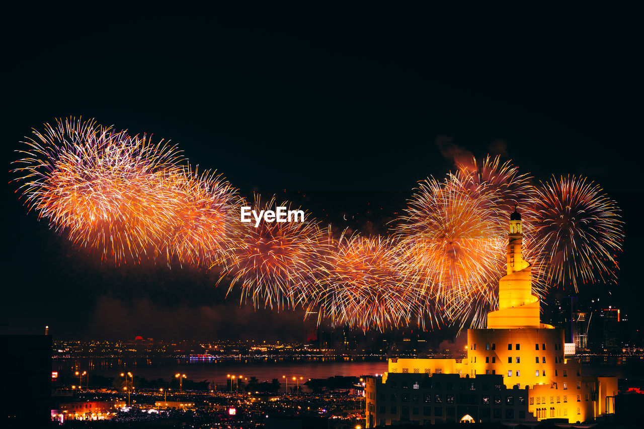 FIREWORK DISPLAY OVER ILLUMINATED BUILDINGS AGAINST SKY