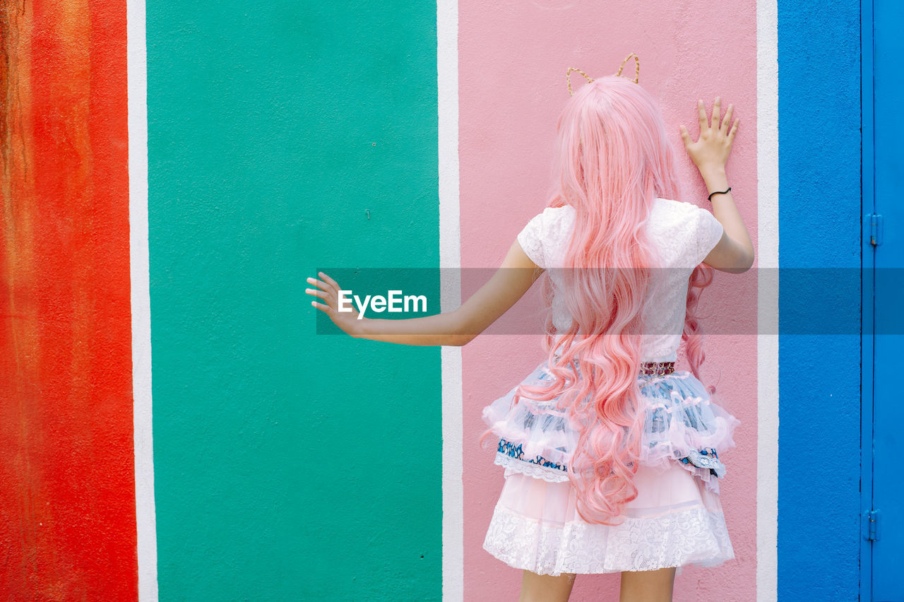 Rear view of woman standing against colored wall