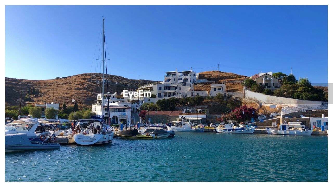 SAILBOATS MOORED ON RIVER BY BUILDINGS AGAINST BLUE SKY