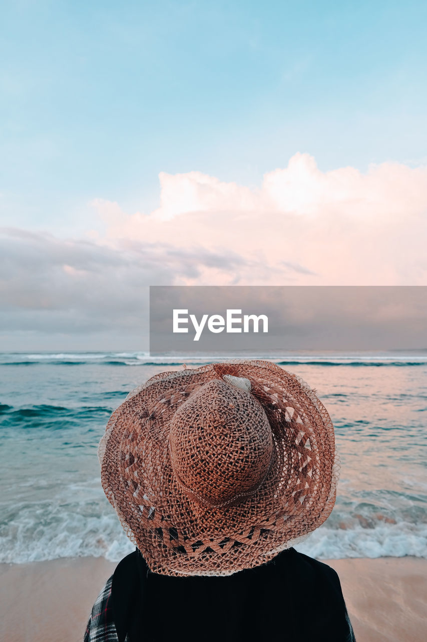 Rear view of woman wearing hat at beach against sky