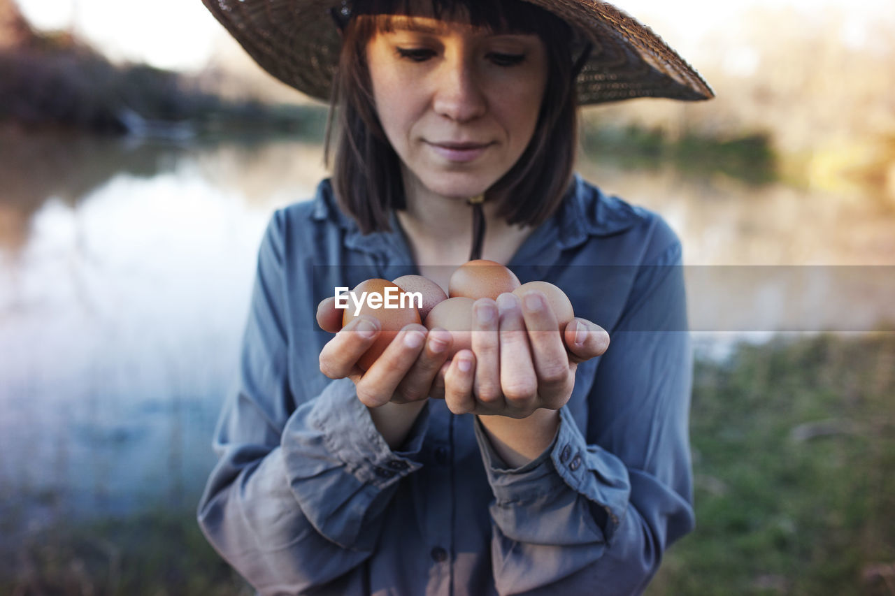 Young female farmer holding eggs while standing on lakeshore