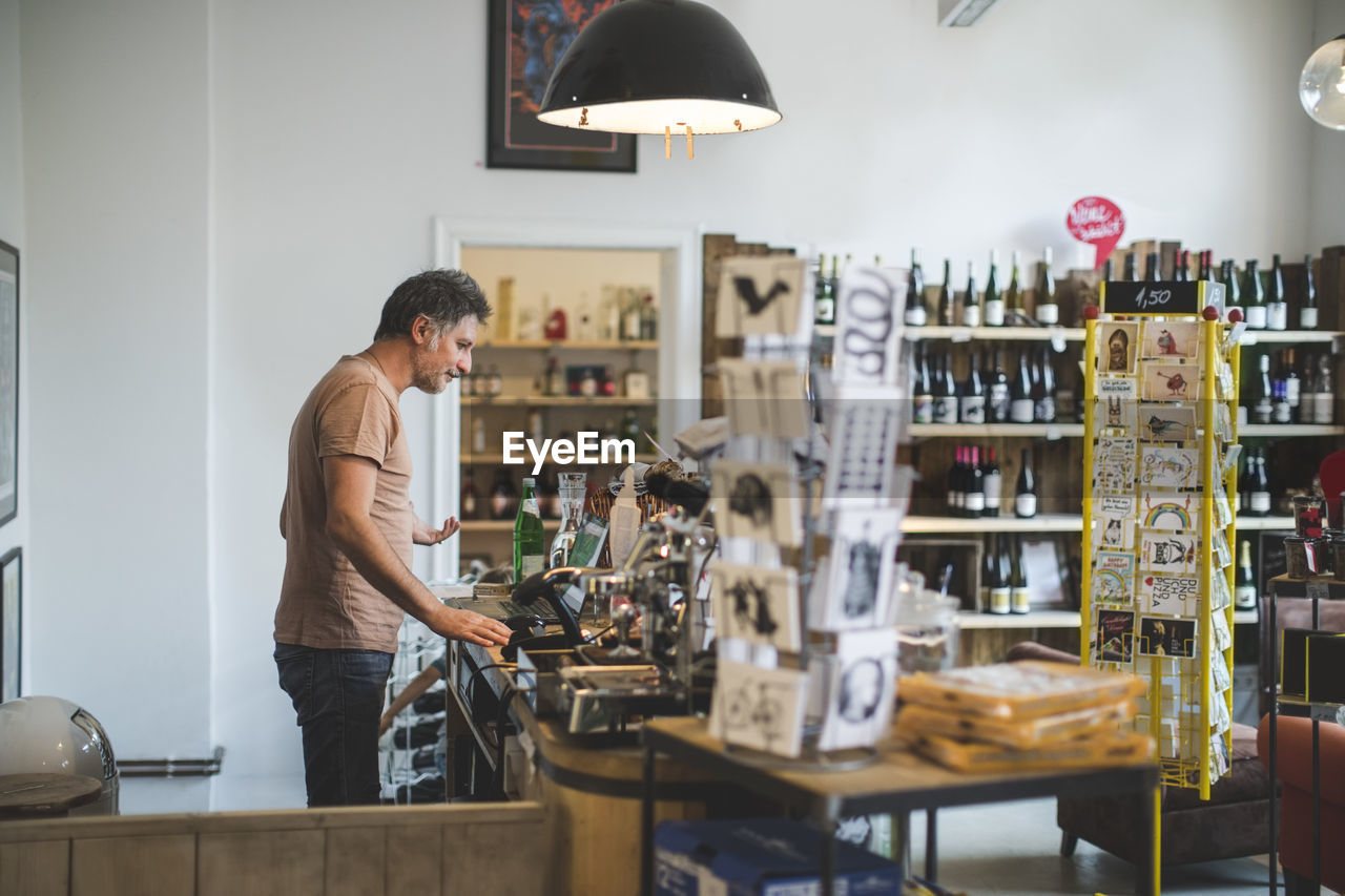 Side view of male sales clerk standing at checkout counter in deli