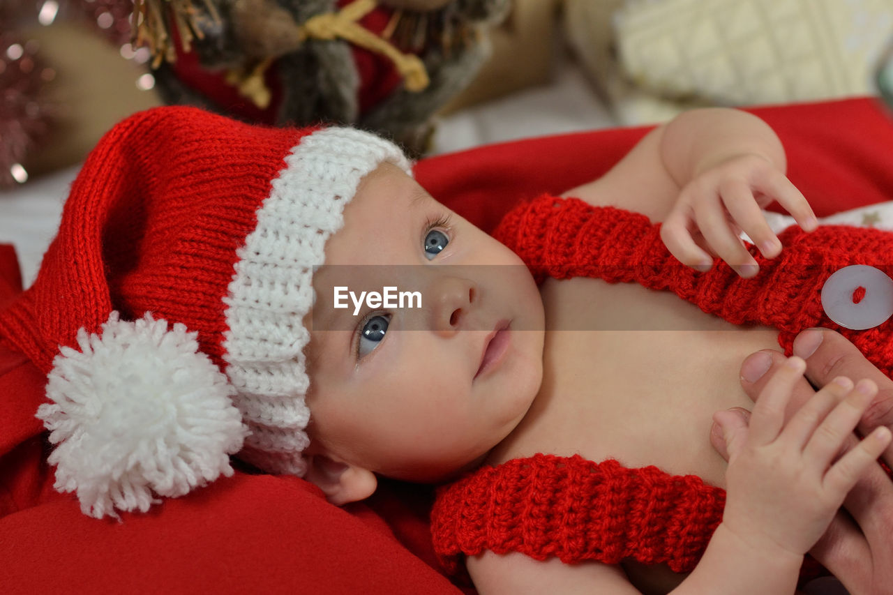 child, childhood, baby, red, lying down, portrait, one person, cute, christmas, indoors, clothing, innocence, hat, holiday, toddler, person, looking at camera, emotion, celebration, winter, pink, headshot, happiness, furniture, relaxation, lifestyles, domestic room, nature, smiling, comfortable, blanket, positive emotion, christmas tree, babyhood, home interior, front view, skin, close-up