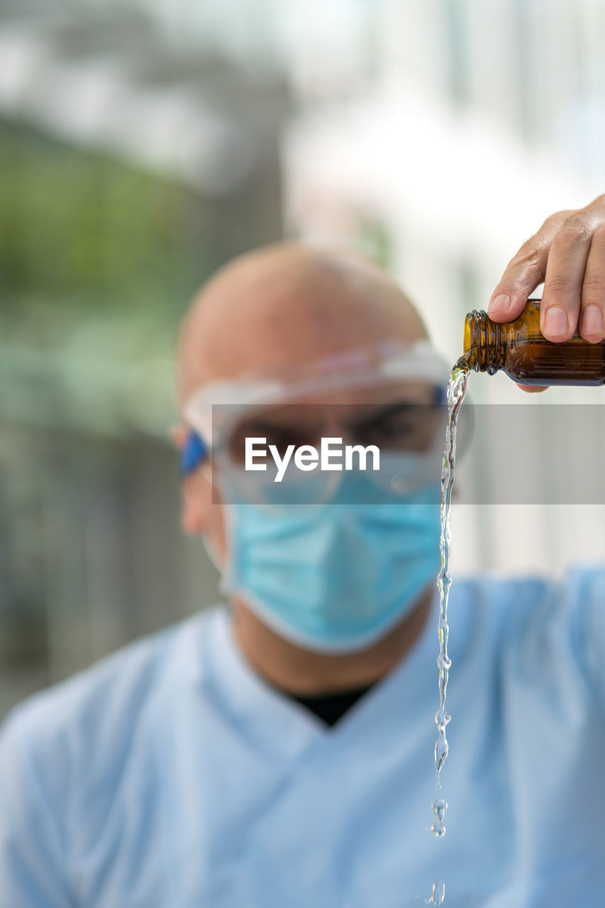 Doctor wearing protective mask and medical safety goggles holding a bottle pouring medical syrup