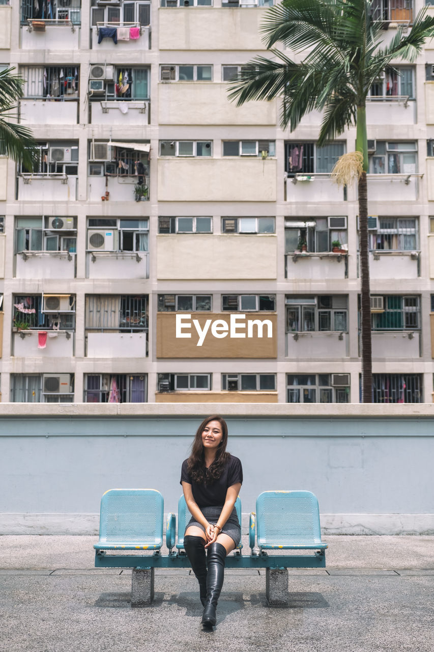 FULL LENGTH PORTRAIT OF WOMAN SITTING AGAINST BUILDING