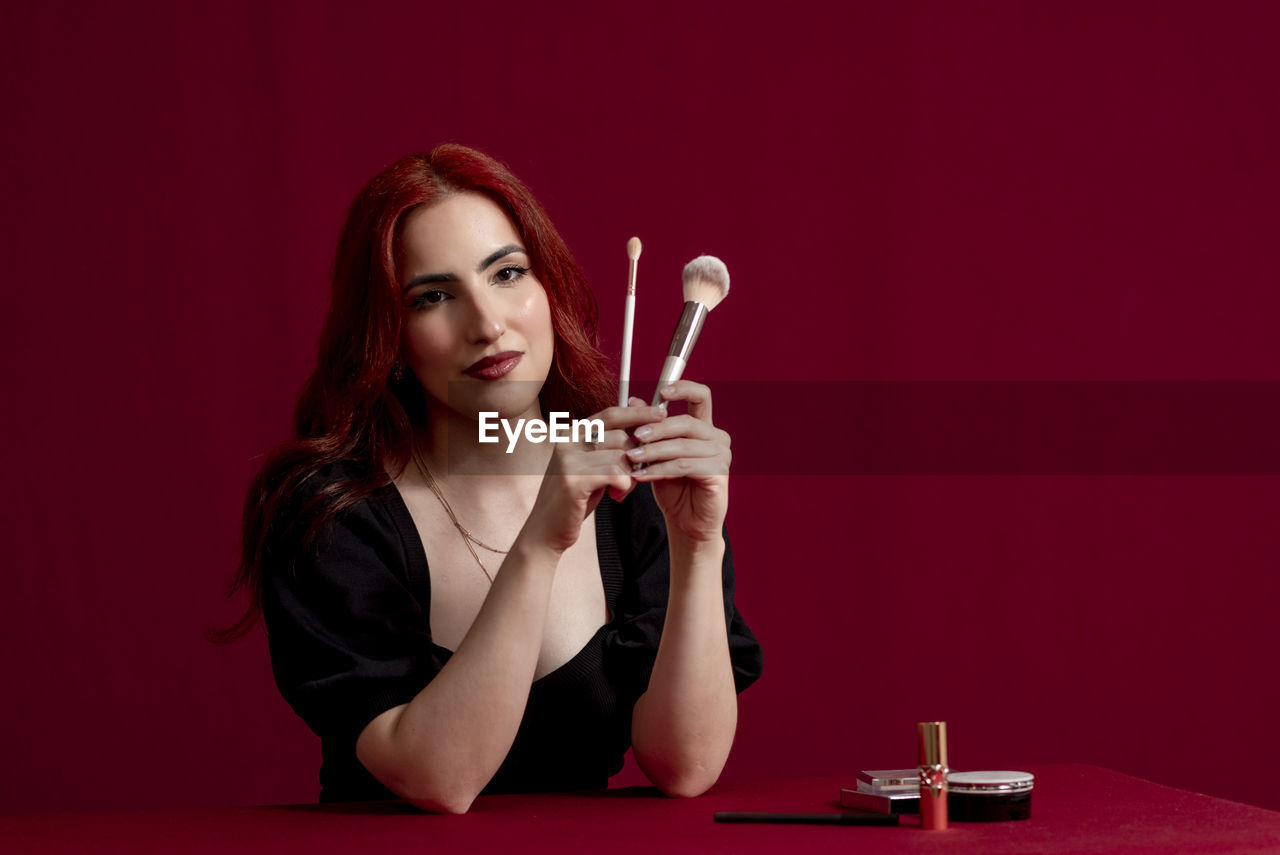 Woman smiling while holding makeup brushes standing against an isolated background.