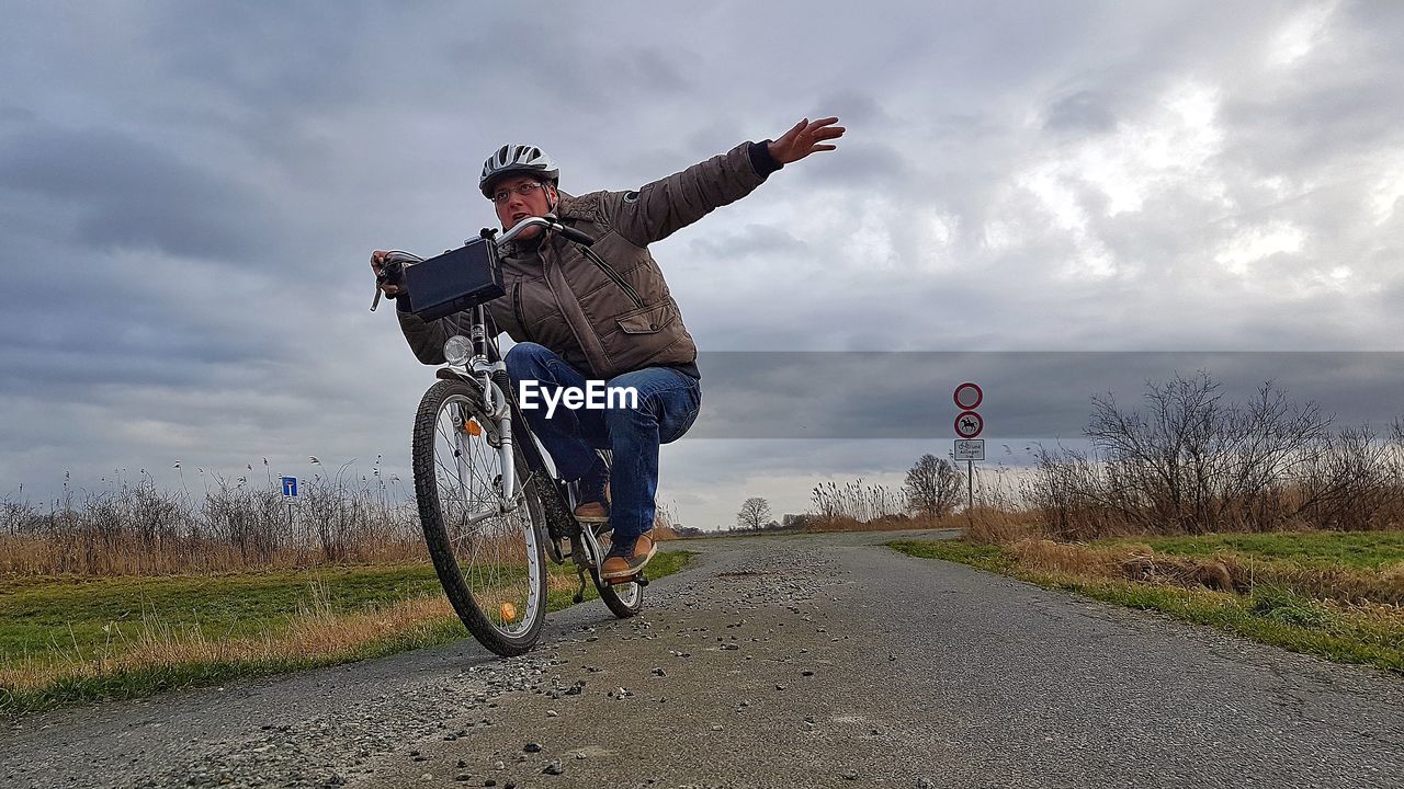 MAN RIDING BICYCLE BY ROAD AGAINST SKY