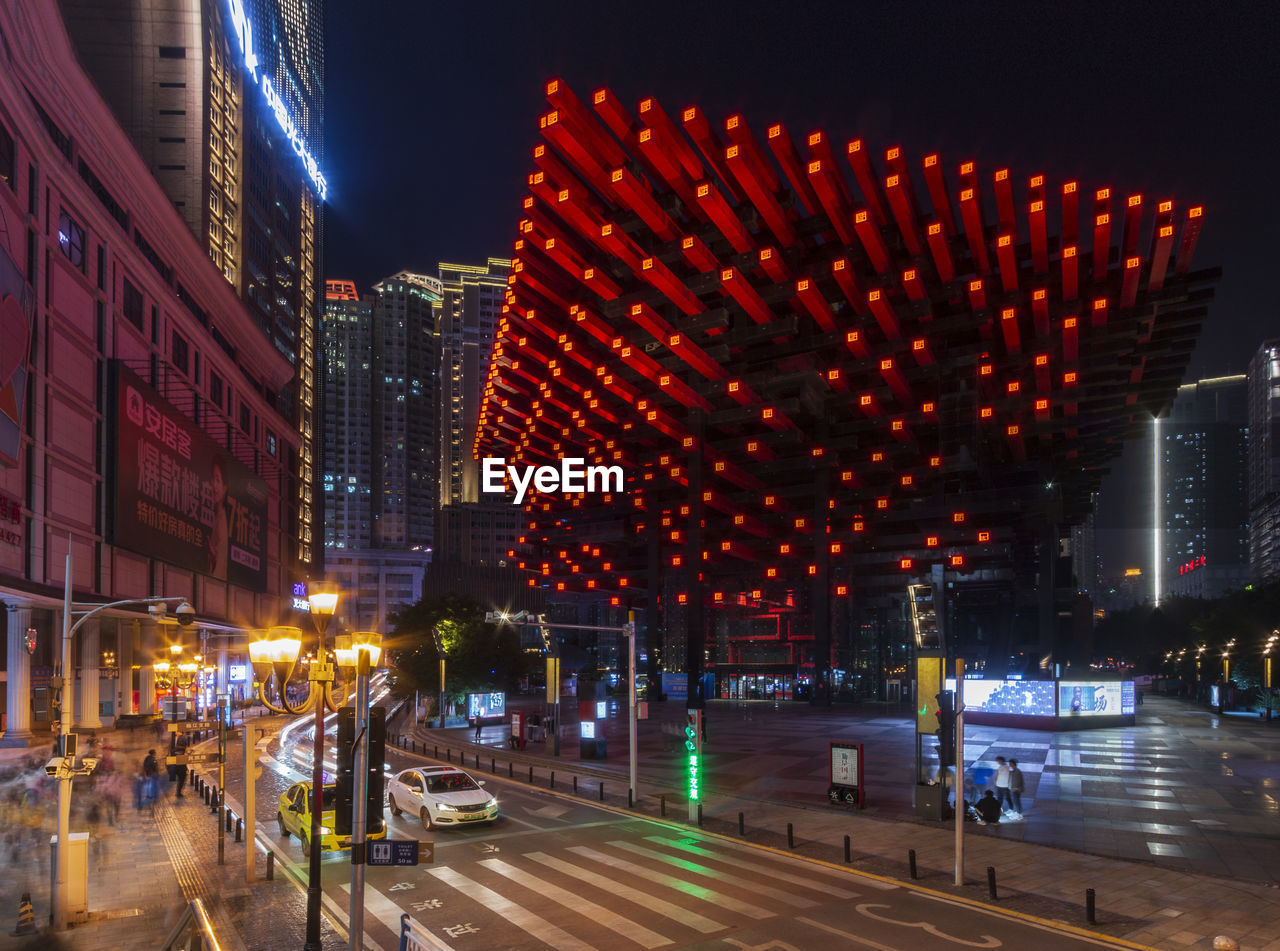 ILLUMINATED CITY STREET AMIDST BUILDINGS AT NIGHT