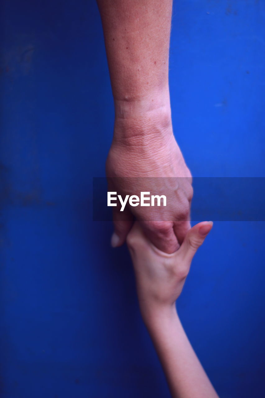 Cropped image of parent and baby holding hands against blue background