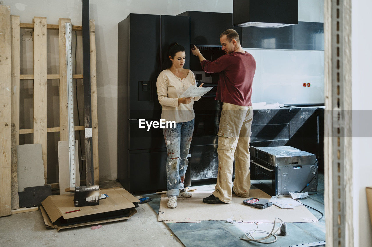 Couple discussing over document while fixing cabinet together in kitchen during home renovation
