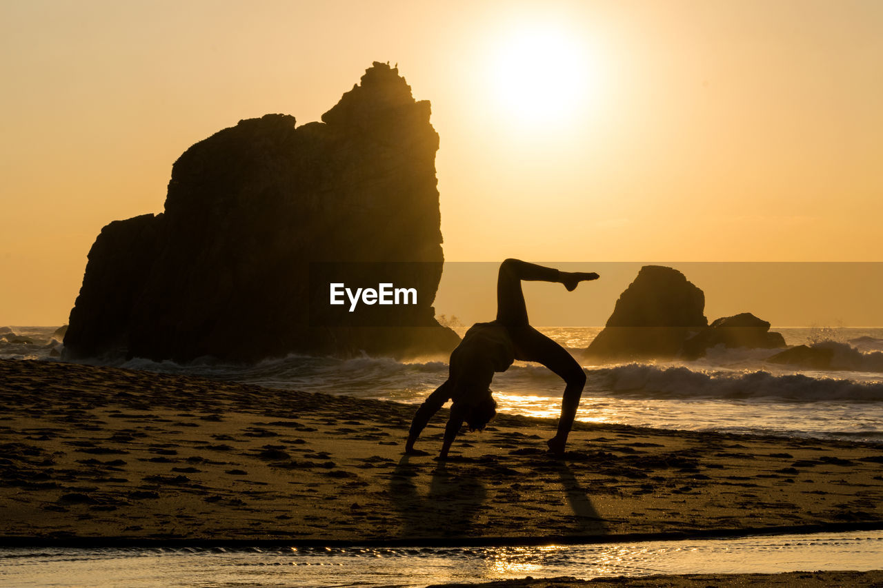 Silhouette of woman doing yoga on beach at sunset