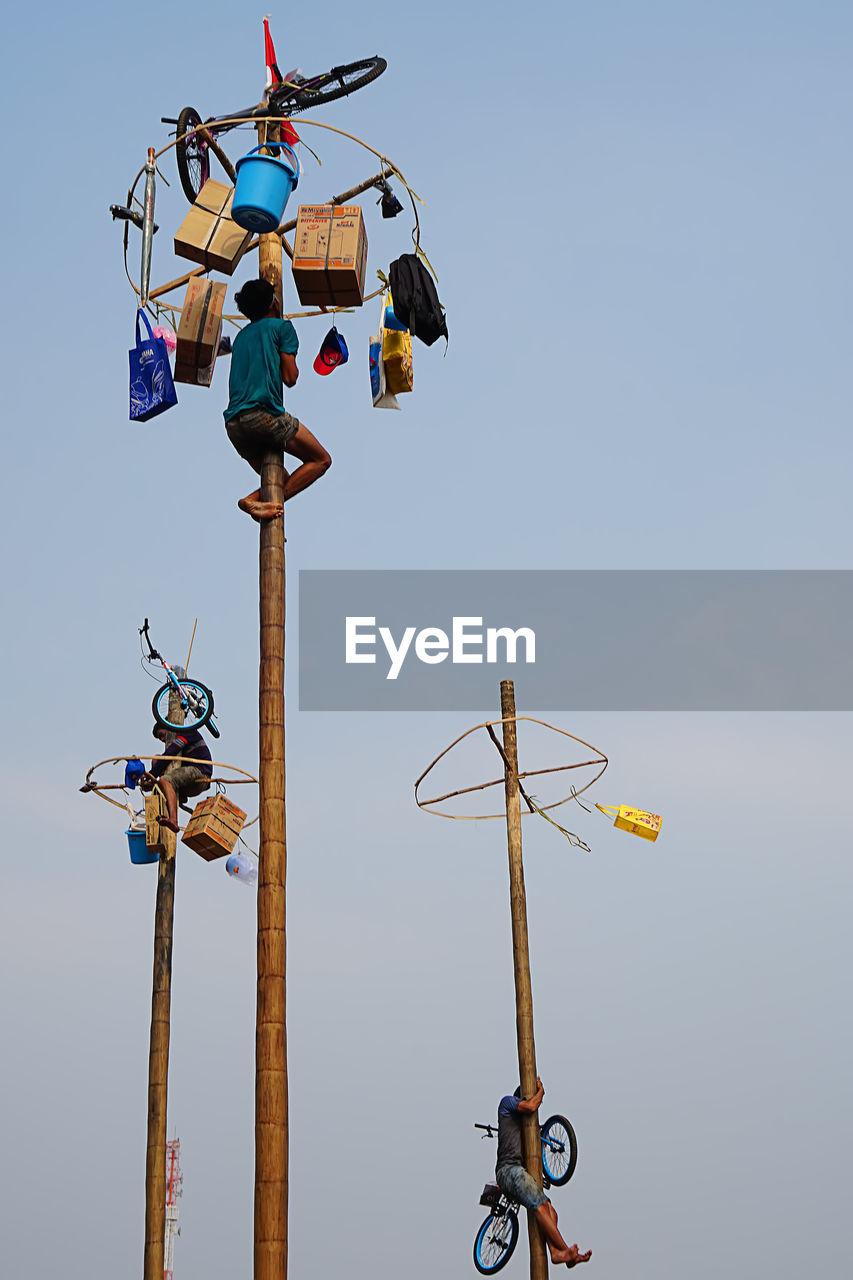 Low angle view of people climbing on poles against sky during sunset