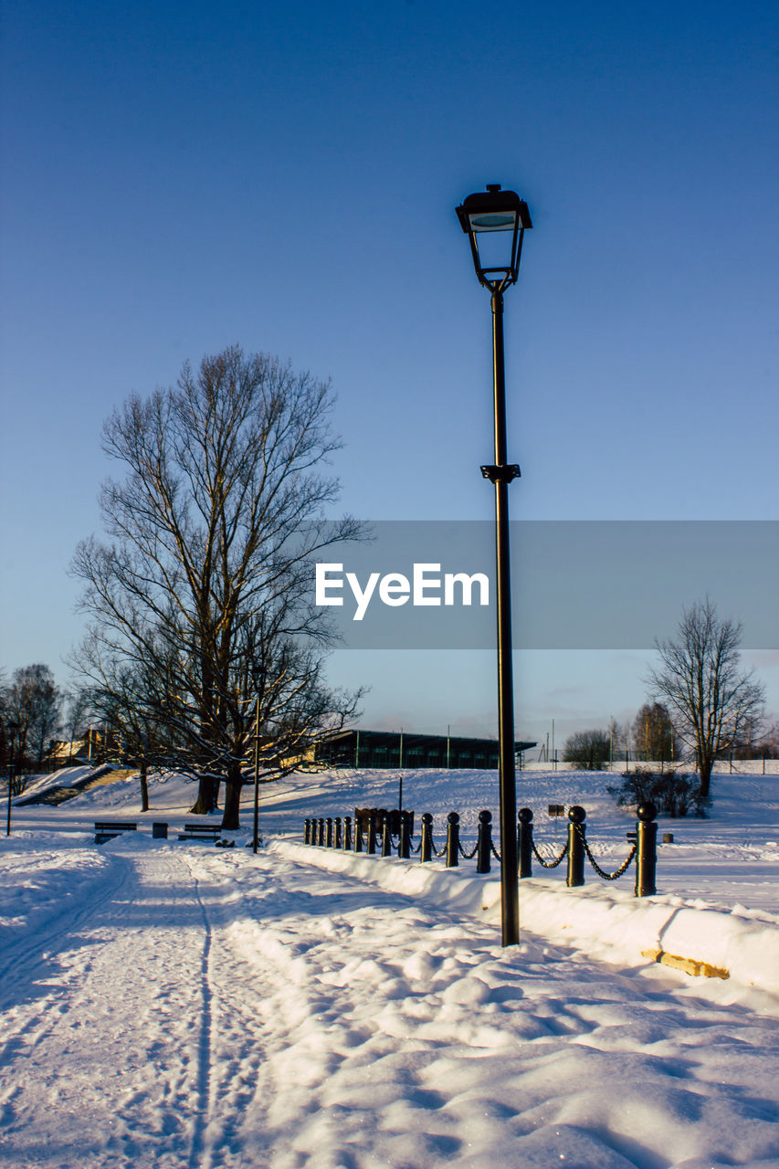 STREET LIGHT ON SNOW COVERED FIELD AGAINST BLUE SKY