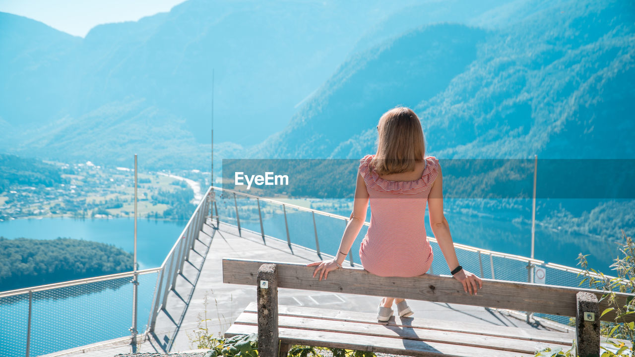 REAR VIEW OF WOMAN LOOKING AT SEA BY MOUNTAINS