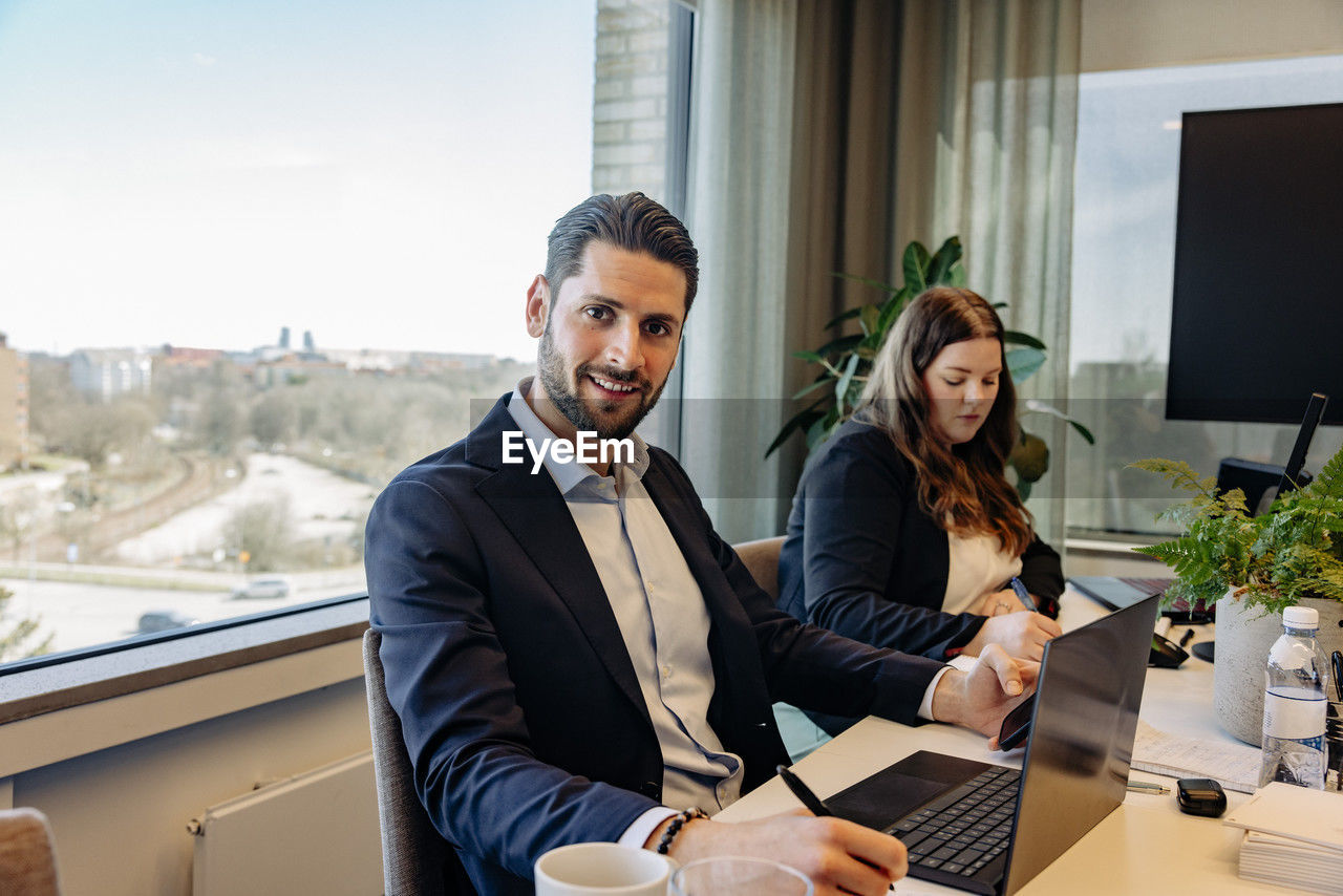 Portrait of smiling businessman sitting with colleague at desk in coworking office