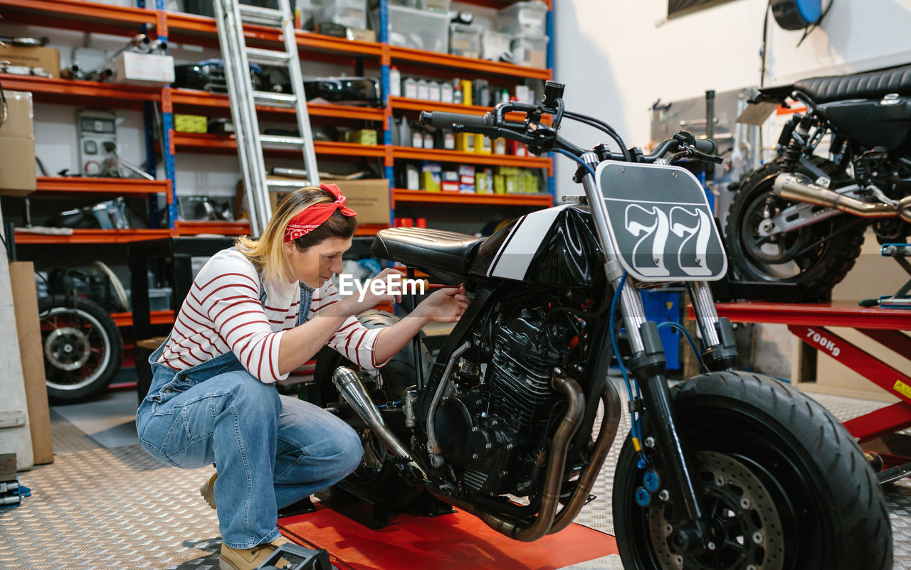 Mechanic woman repairing custom motorcycle on factory