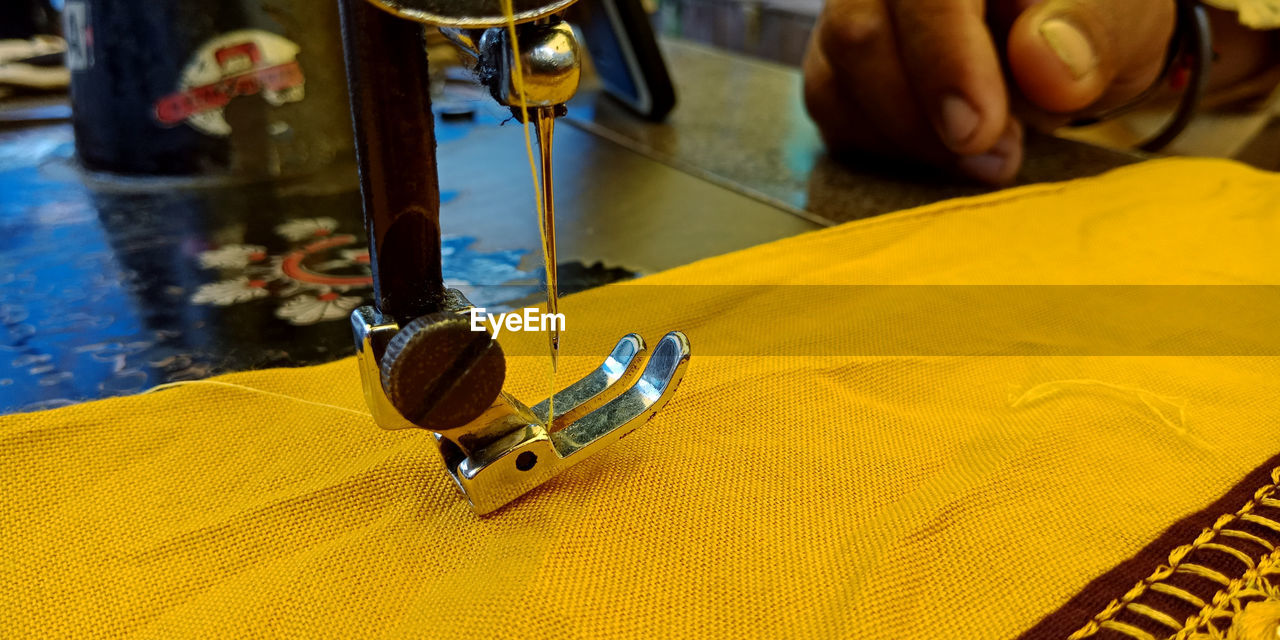 Cropped hand sewing yellow textile on machine