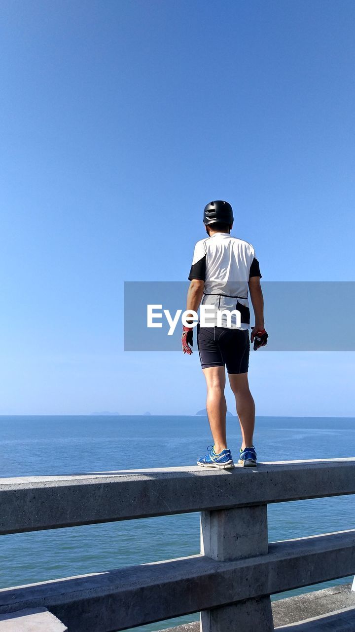 Rear view full length of man standing by sea on railing