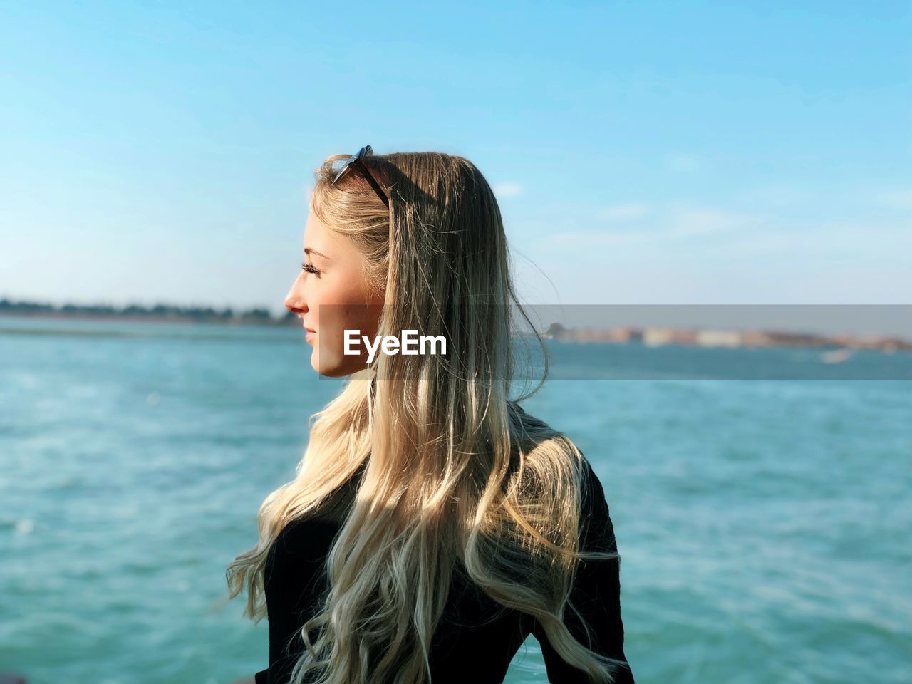 Young woman looking away while standing by sea against sky