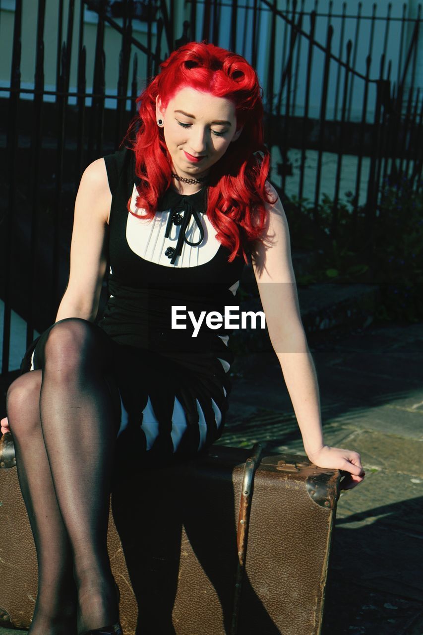 Smiling redhead woman sitting on old-fashioned suitcase