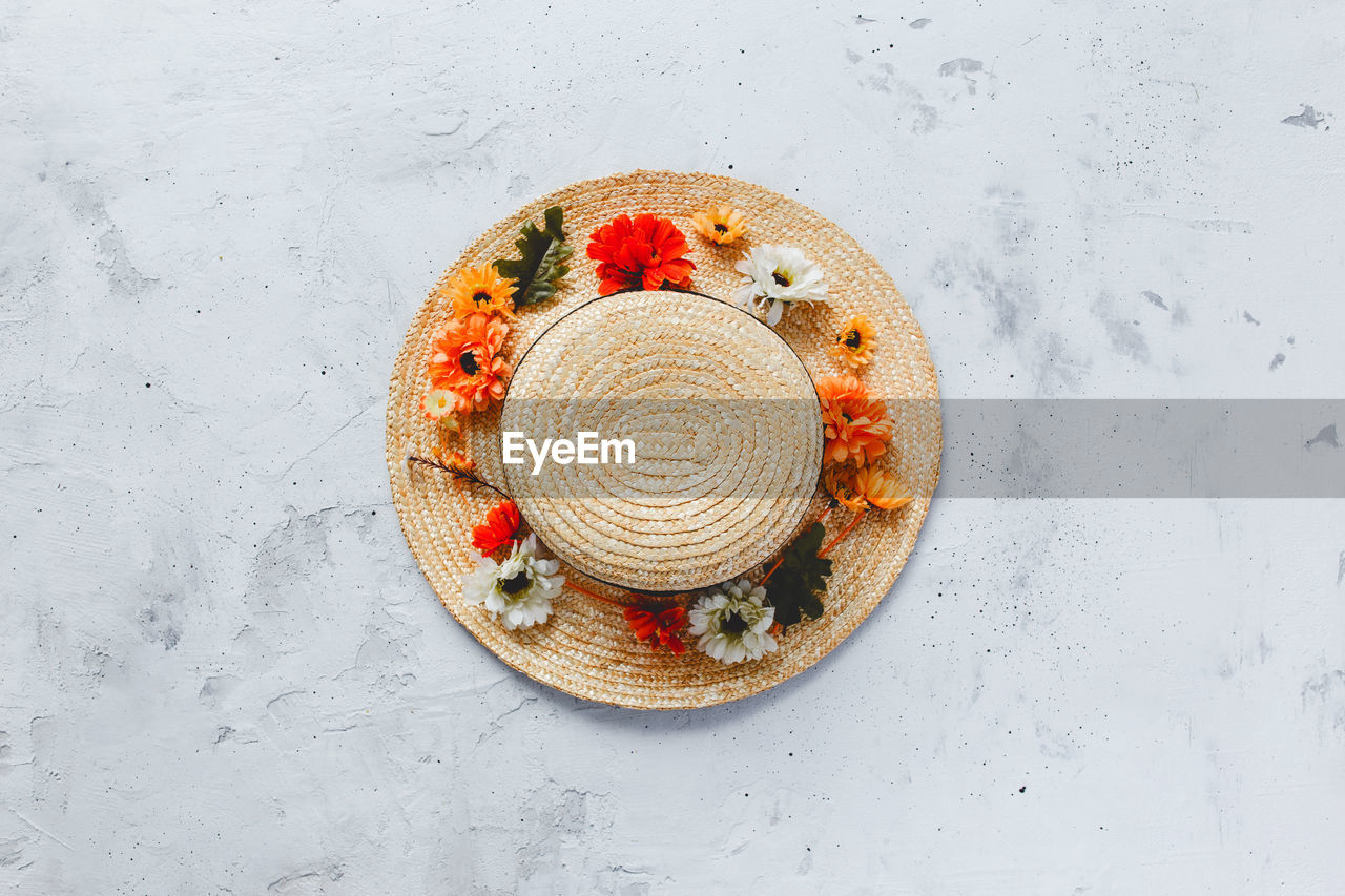 Grey concrete flat lay background with colorful autumn flower heads on straw hat