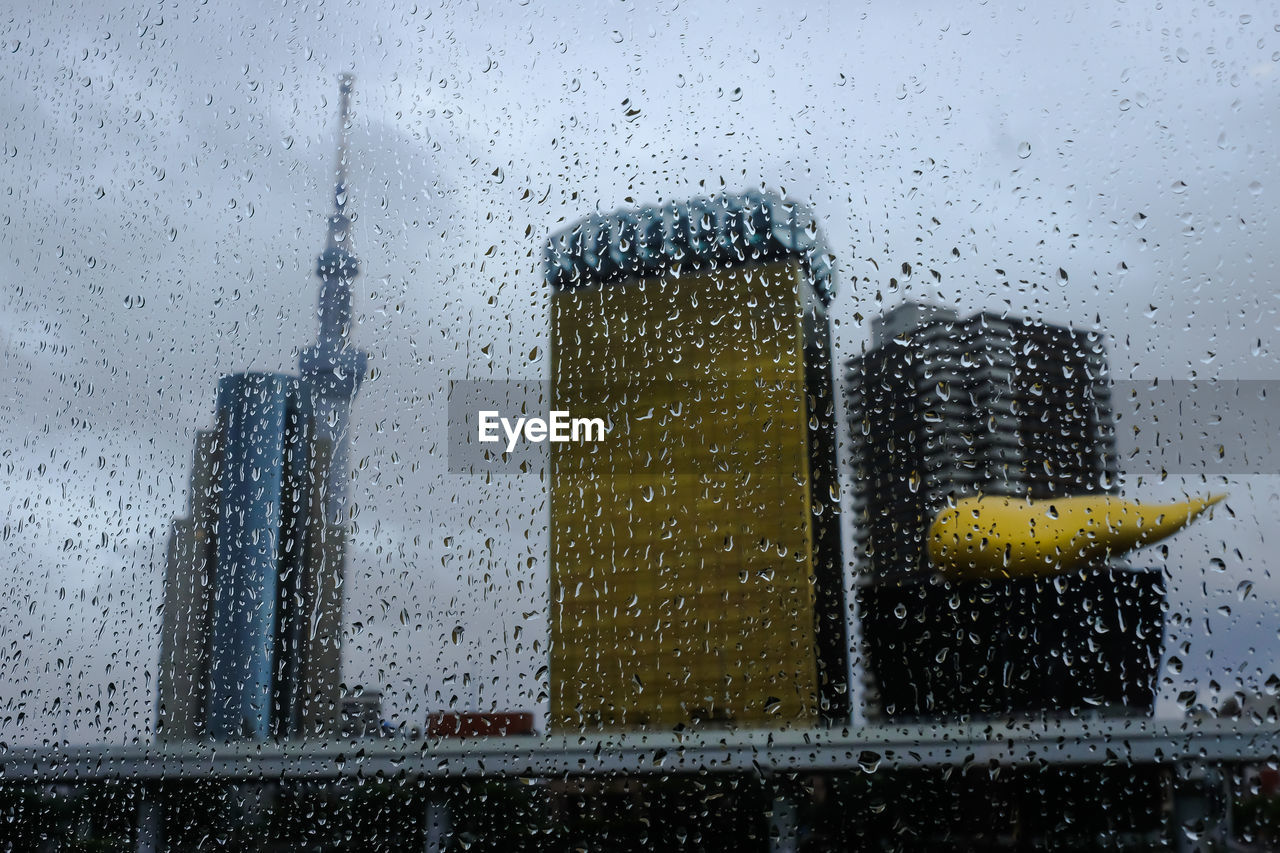 Low angle view of tokyo skytree and buildings seen through wet window