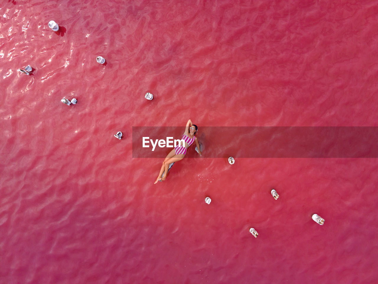 Woman in a striped bathing suit lies on a pink lake taken from above from a drone