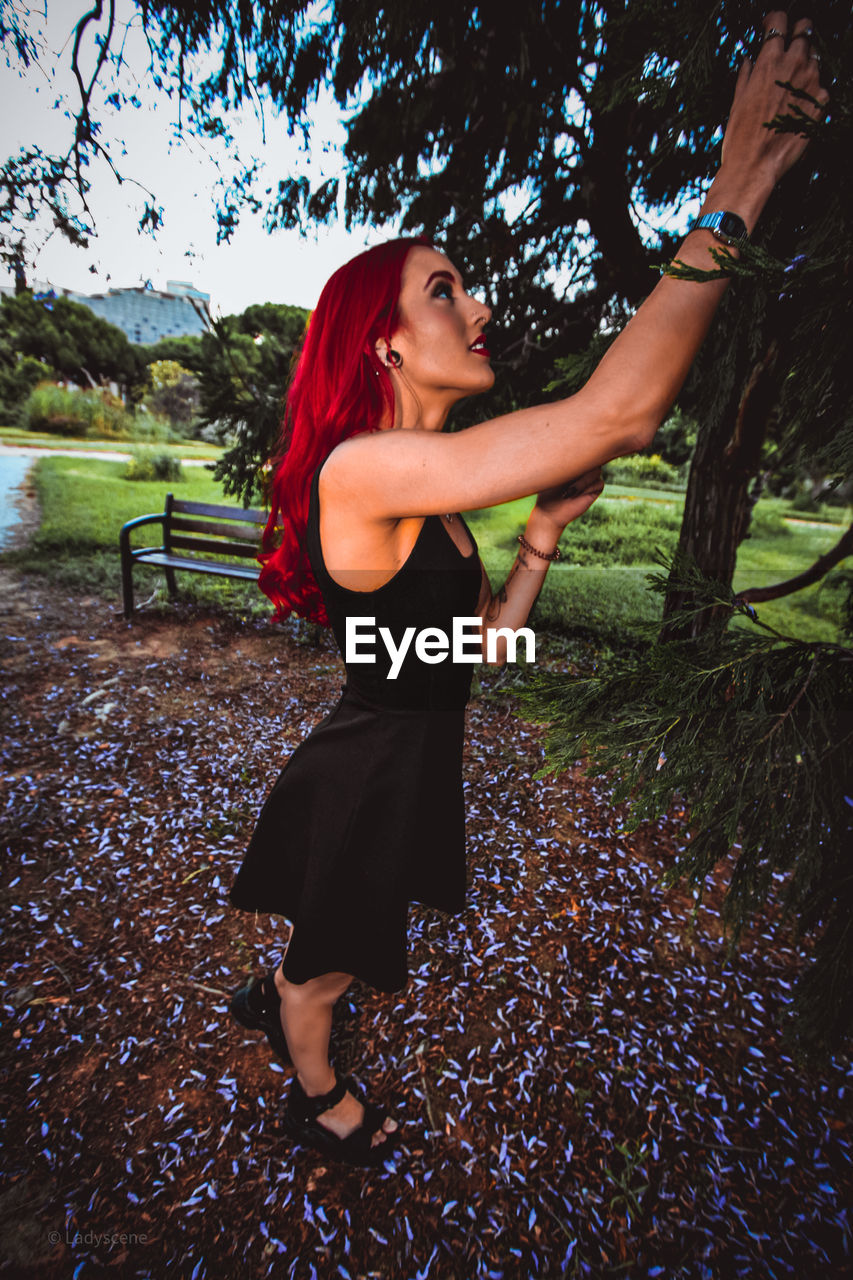 Side view of young woman standing against trees