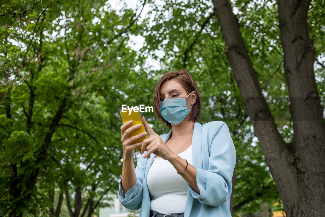 WOMAN HOLDING UMBRELLA STANDING AGAINST PLANTS