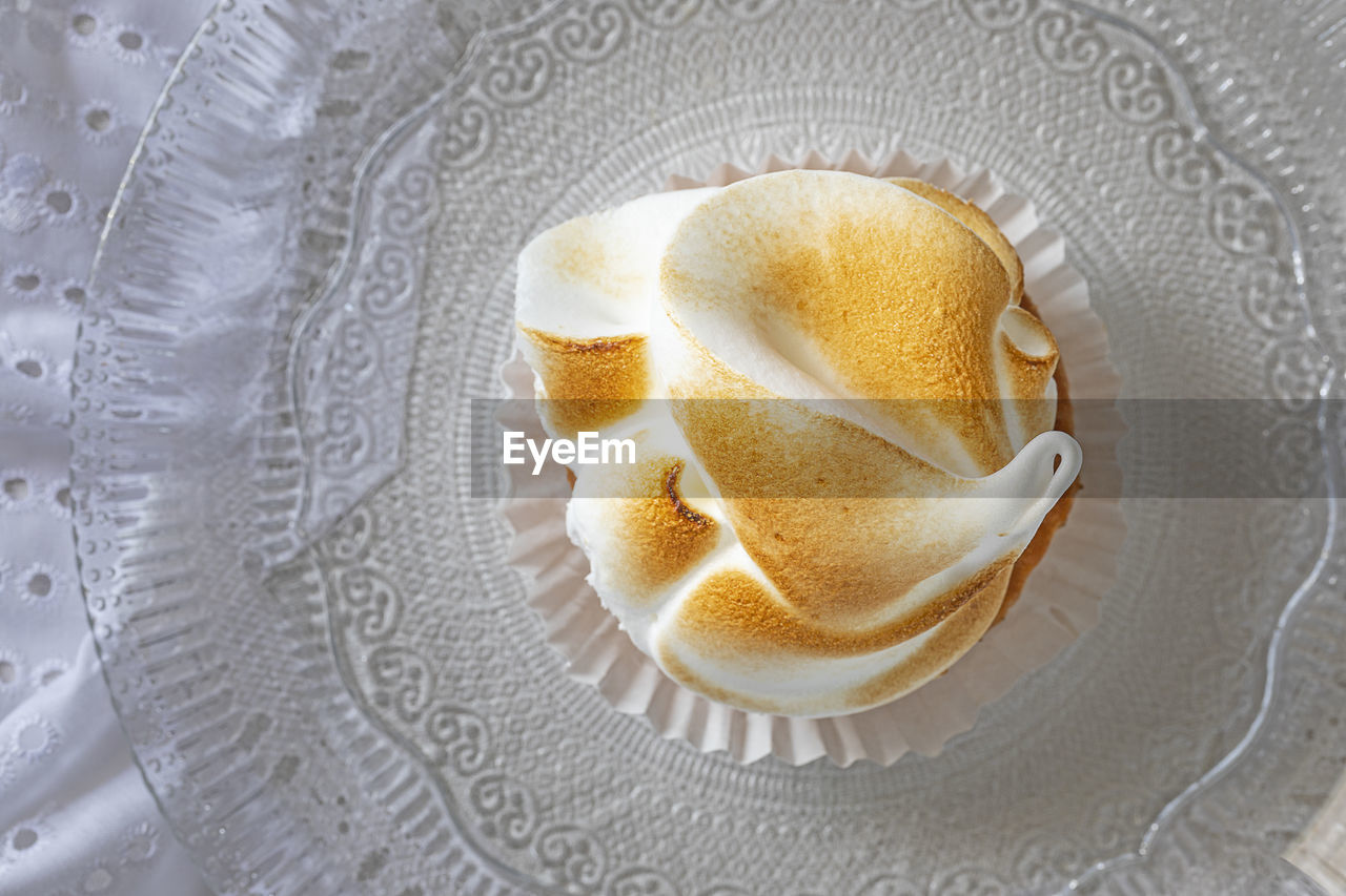 Lemon meringue tartlet on a transparent plate.