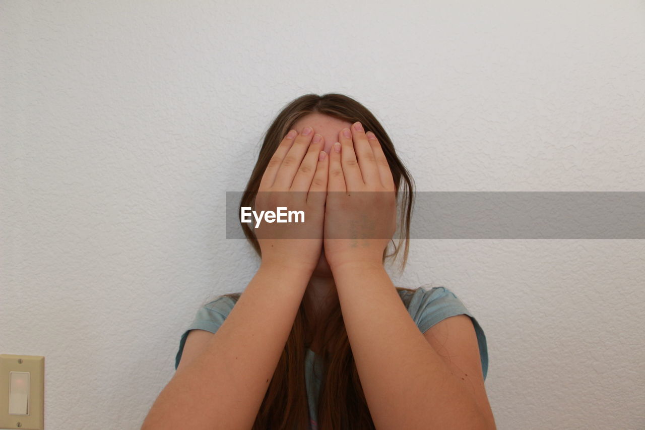 Teenage girl covering face against white wall