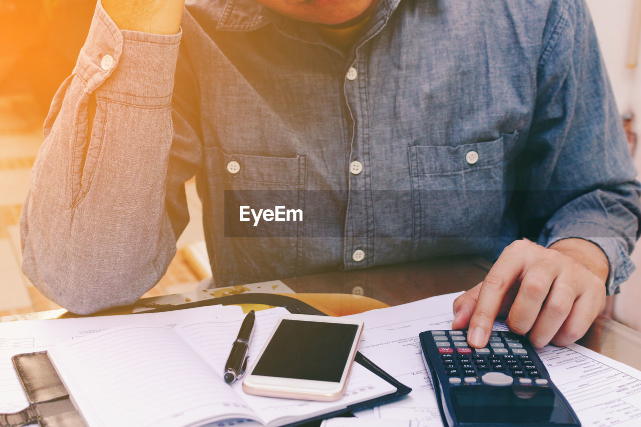 Midsection of man with calculating on desk at office