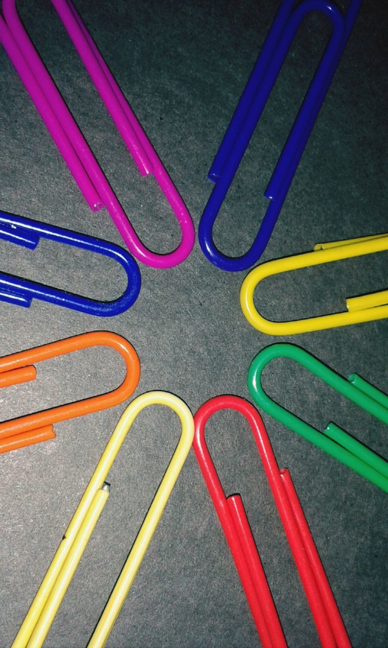 Directly above view of multi colored paper clips forming circle against gray background