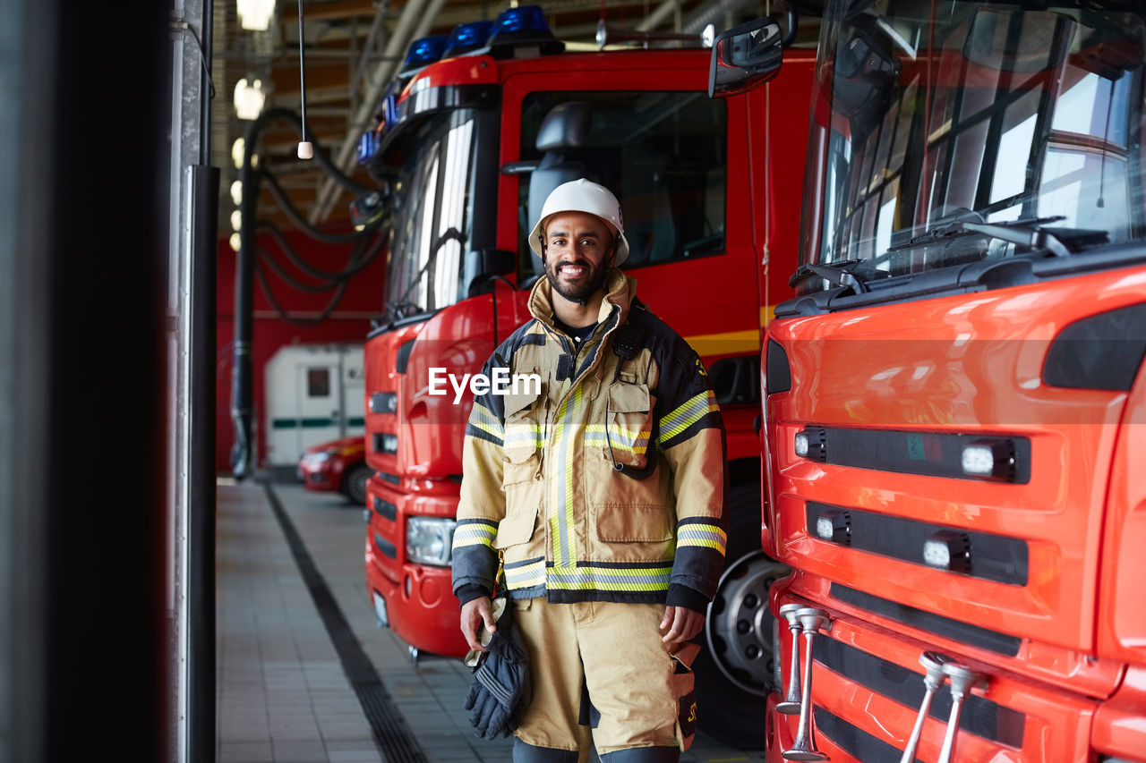 Portrait of smiling firefighter standing by fire engine at fire station