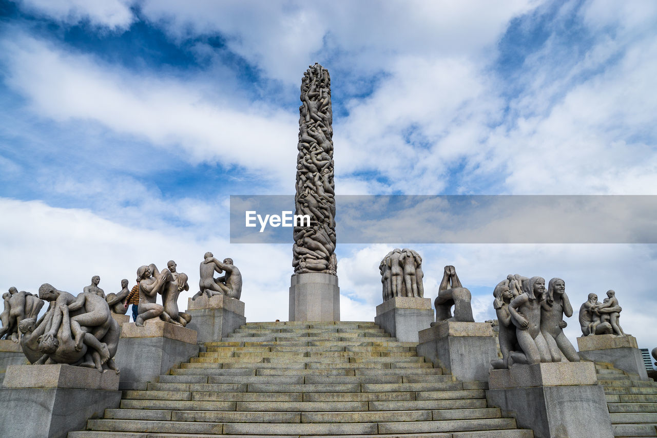 Low angle view of sculptures at gustav vigeland sculpture park against cloudy sky