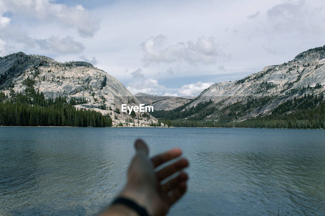 Cropped hand of man against lake by mountains