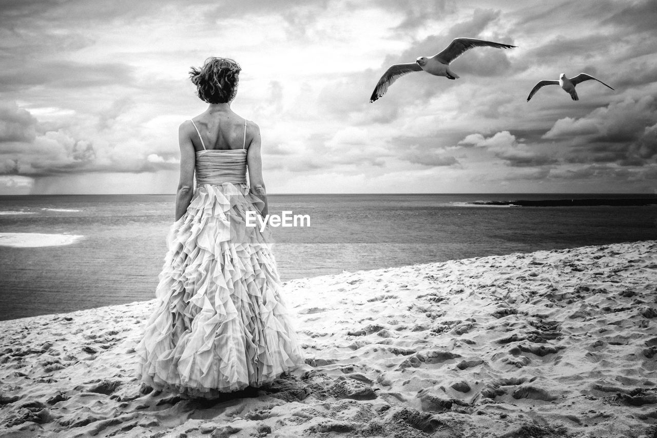 Rear view of woman wearing evening gown standing on beach