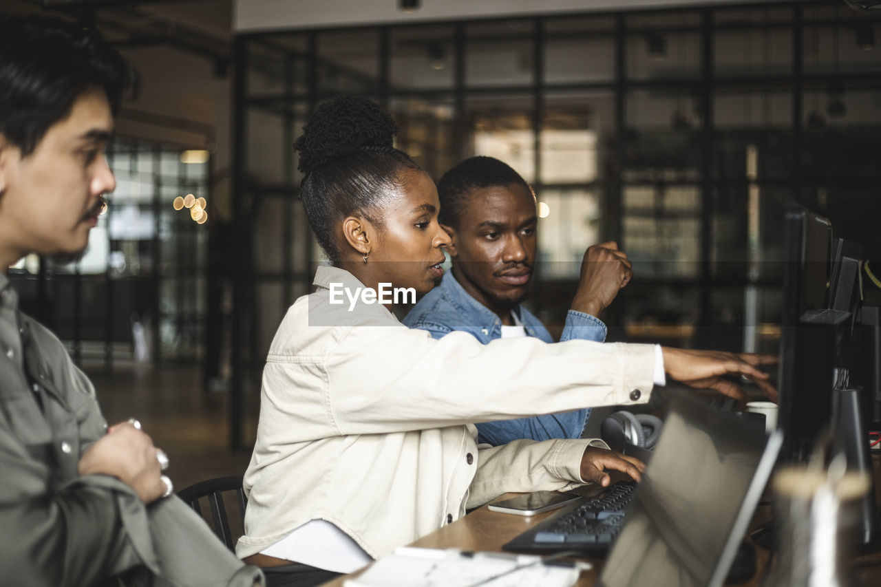 Businesswoman discussing with male colleague over computer at startup company