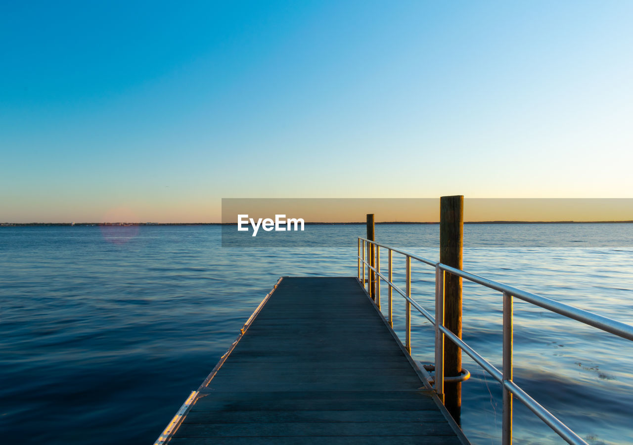 Pier over sea against clear sky during sunset