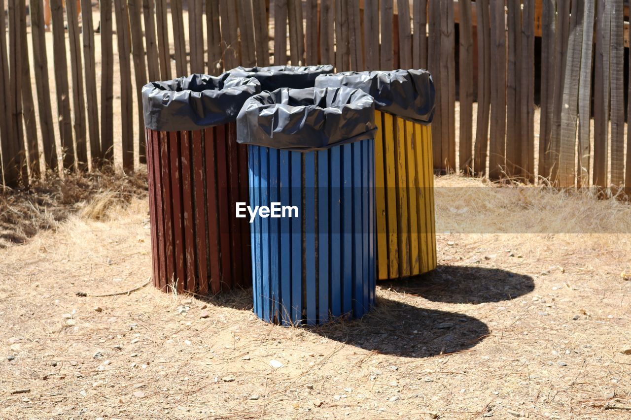 High angle view of trash cans against wooden fence on sunny day