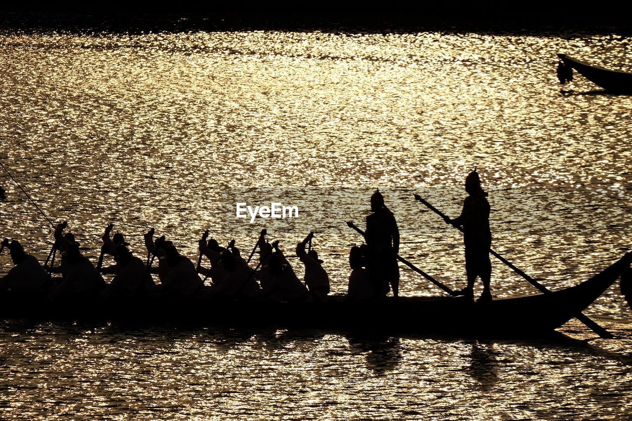 SILHOUETTE PEOPLE BY BOATS ON SEA AGAINST SKY