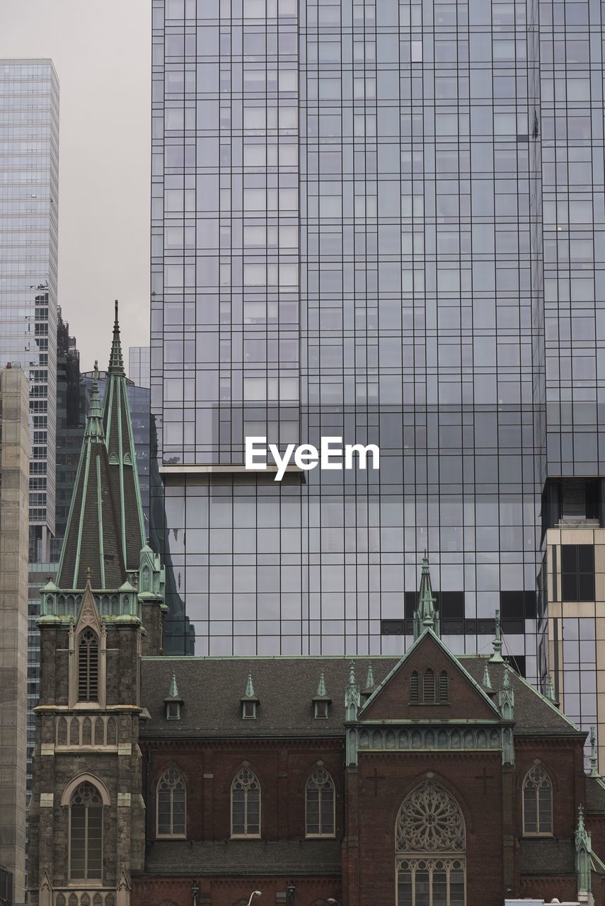 Old church with stone facade on background of contemporary tall skyscraper with glass mirrored walls in new york